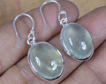 May include: A pair of silver earrings with oval-shaped green gemstones. The earrings have a simple design and are perfect for everyday wear.