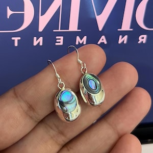 May include: A pair of silver earrings with oval-shaped abalone shell inlays. The earrings have a silver hook fastening.