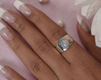 May include: A silver ring with a large oval opal gemstone. The opal has a rainbow of colors, including green, blue, and pink.