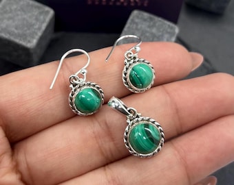 Puede incluir: Un conjunto de pendientes y un colgante de plata de ley con piedras de malaquita verde. Las piedras están engastadas en un engaste de plata con un borde de cuerda.