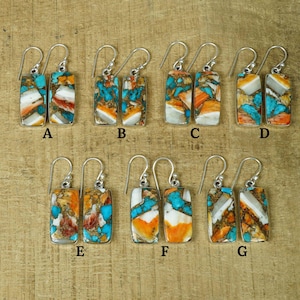以下が含まれることがあります： ターコイズと茶色の石のインレイが施された長方形のシルバー製ドロップイヤリングが7ペア。イヤリングにはAからGまでのラベルが付けられています。
