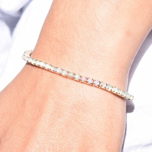 May include: A delicate gold bracelet with a row of white opal stones. The bracelet is on a person's wrist.
