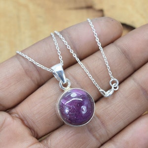 May include: A silver chain necklace with a round purple gemstone pendant.