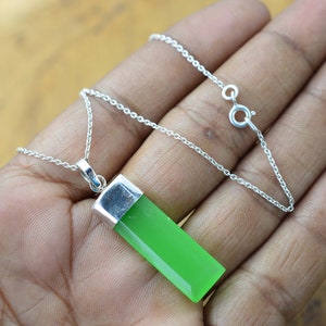Könnte beinhalten: Eine silberne Kettenkette mit einem grünen Edelstein-Anhänger. Der Anhänger ist rechteckig und hat eine glatte, polierte Oberfläche.