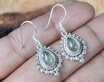 May include: A pair of silver dangle earrings with green gemstone drops. The earrings feature a detailed silver design with a teardrop-shaped gemstone in the center.