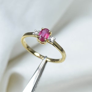 May include: A gold ring featuring a pink oval ruby gemstone and two smaller diamond accents.