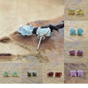 May include: A set of 10 pairs of raw gemstone earrings. Each pair features a different color of gemstone, including aquamarine, green, pink, and red. The earrings are made with sterling silver posts and are perfect for adding a touch of natural beauty to any outfit.