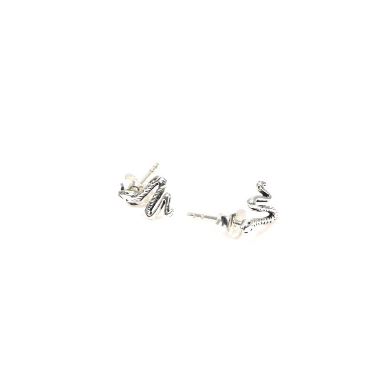 May include: A pair of silver-colored stud earrings. Each earring is shaped like a small snake with detailed scales and a curved body. The earrings are set against a white background.
