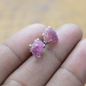 以下が含まれることがあります： ピンクの原石のアクセントが付いたシルバーのイヤリングのペア。イヤリングはシンプルでミニマルなスタイルで設定されています。