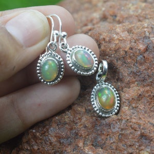 Puede incluir: Un conjunto de pendientes y un colgante de plata con piedras preciosas de &oacute;palo de forma ovalada. Los pendientes tienen un dise&ntilde;o simple de gota y el colgante tiene una cadena delicada.