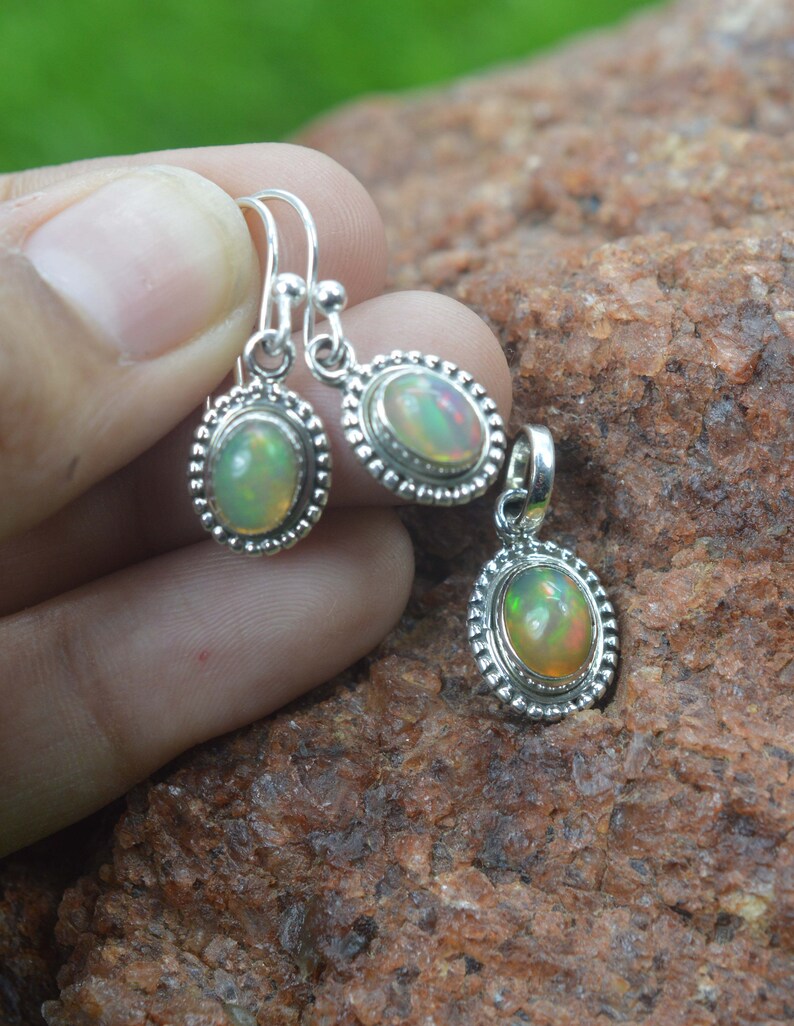 Puede incluir: Un conjunto de pendientes y un colgante de plata con piedras preciosas de &oacute;palo de forma ovalada. Los pendientes tienen un dise&ntilde;o simple de gota y el colgante tiene una cadena delicada.