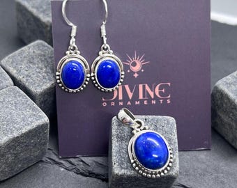 Puede incluir: Un conjunto de joyas con pendientes y un colgante. Cada pieza tiene un engaste de metal plateado con una piedra ovalada azul vibrante. Los pendientes son de estilo colgante, y el colgante cuelga de una fianza plateada. La marca "DIVINE ORNAMENTS" es visible.