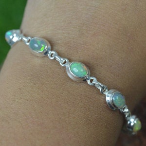 May include: A silver chain bracelet with five oval-shaped opal gemstones. The bracelet is on a person's wrist.
