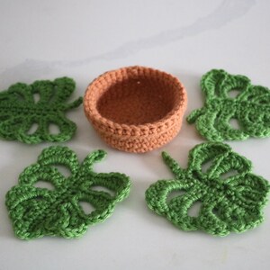 May include: Four green crocheted monstera leaves and a small orange crocheted pot.