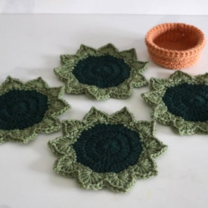 May include: Four green and dark green crocheted coasters with a starburst design. A smaller orange crocheted bowl is in the center of the image.