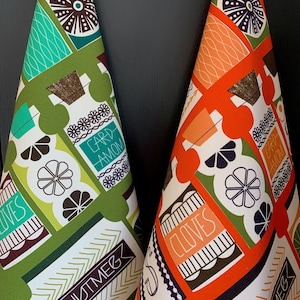 May include: Two kitchen towels with a retro design featuring a geometric pattern of orange, green, white, and brown. The towels have the words "cloves", "nutmeg", "cardamom", and "ginger" printed on them.