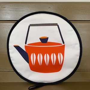 May include: A round orange and white teapot pot holder with a black border and a black handle. The pot holder has the word "cosytime" printed on the bottom.