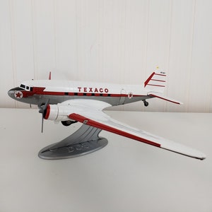 May include: A white and red model airplane with the word "TEXACO" printed on the side. The airplane is on a gray stand and has a red star on the tail.