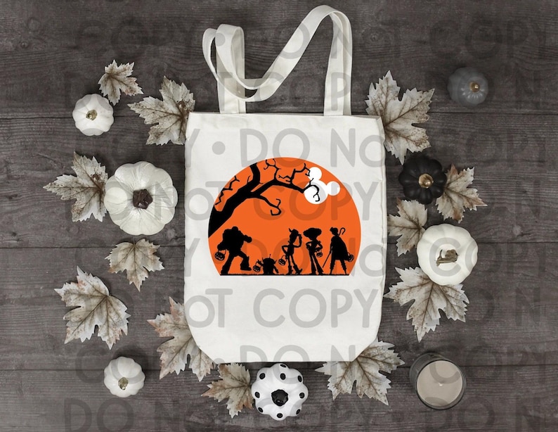 May include: A white canvas tote bag featuring a graphic print of a large orange moon with a black silhouette of a tree and four characters holding trick-or-treat buckets. The design includes a small white mouse-ear shape on the tree branch.