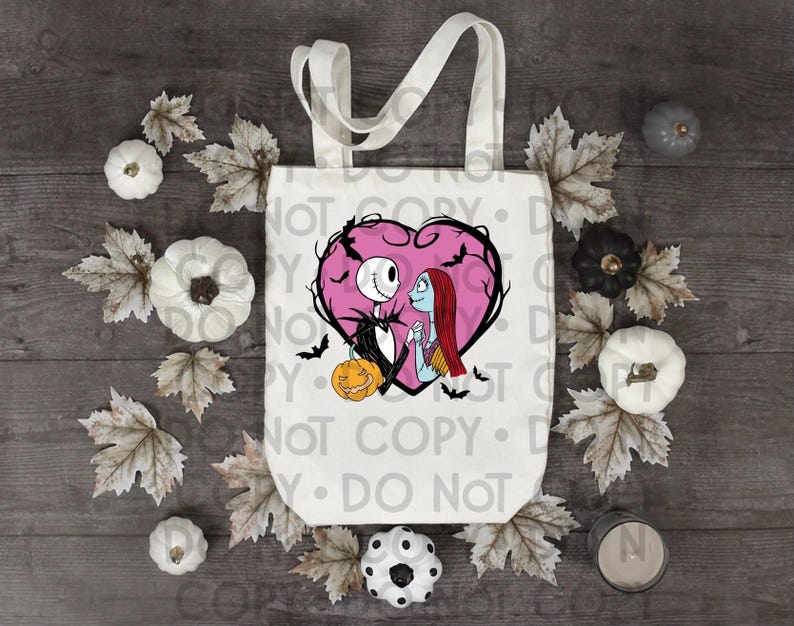 May include: A white canvas tote bag featuring a graphic of Jack Skellington and Sally from The Nightmare Before Christmas inside a pink heart, surrounded by black bats and a small orange pumpkin, with two sturdy top handles for carrying.