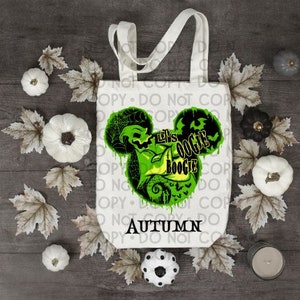 May include: A white tote bag with a green and black graphic of a cartoon character with the text "Let's Oogie Boogie" and "Autumn".
