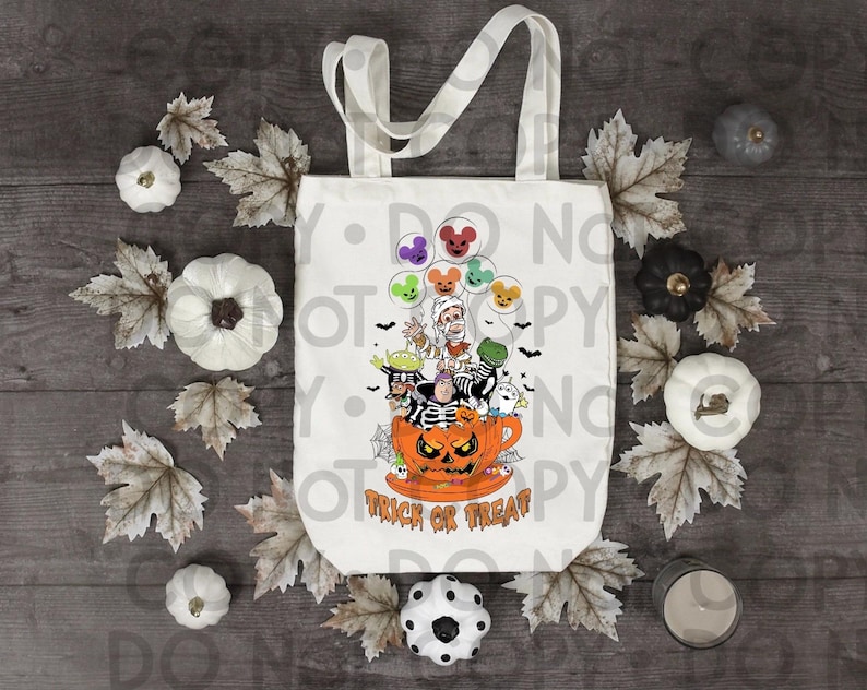 Peut inclure: Un sac fourre-tout en toile blanche orn&eacute; d'un motif de personnages de dessins anim&eacute;s dans une tasse citrouille, entour&eacute;s de ballons en forme de souris, de chauves-souris et de toiles d'araign&eacute;e, avec le texte orange "TRICK OR TREAT" en bas.