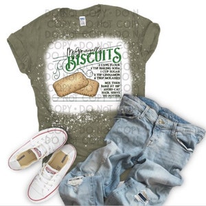 May include: A green bleached t-shirt with a white design that says "Megonagallis Biscuits" and includes a recipe for biscuits. The recipe includes ingredients like flour, baking soda, sugar, cinnamon, and molasses. The design also includes two illustrated biscuits.