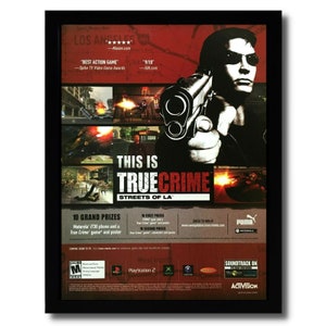 May include: Framed poster for the video game "True Crime: Streets of LA." The poster features a man holding a gun, game screenshots, and the game's title. Includes logos for PlayStation 2, Xbox, and Activision.