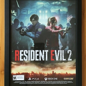 May include: A framed poster for the video game Resident Evil 2. The poster features two characters, a man and a woman, holding guns. The background is a city at night. The poster is framed in black and has a rating of M for Mature.