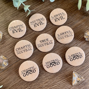 May include: Nine round brown paper buttons with black text and gold accents. The buttons feature different alignment combinations of the words "Chaotic", "Neutral", "Lawful", "Good", "Evil", and "True".