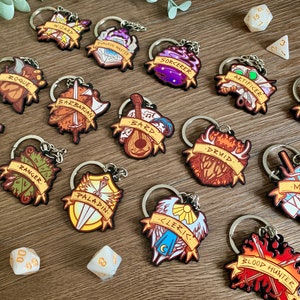 May include: A set of 15 colourful keychains featuring different Dungeons and Dragons character classes. Each keychain has a unique design with a class name and a symbol representing the class. The keychains are made of wood and have a silver metal ring.