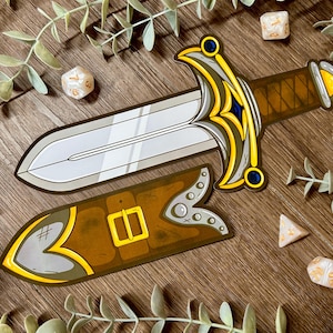 May include: A decorative sword and sheath set with a silver blade, brown handle, and gold detailing. The brown sheath features a gold buckle. Dice are scattered around the sword, suggesting a tabletop game theme.