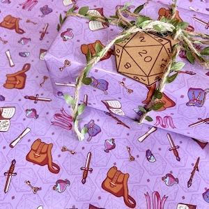 May include: Purple wrapping paper with a repeating pattern of fantasy RPG elements like swords, potions, and dice. A wrapped gift is adorned with twine, faux greenery, and a wooden D20 die tag.