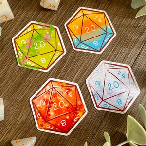 May include: Four hexagonal stickers featuring 20-sided dice designs. One is yellow with green vines, one is orange and blue, one is red with autumn leaves, and one is white with blue snowflakes. Each sticker displays numbers including a central 20.
