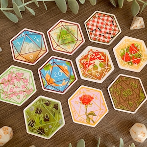 May include: A collection of nine hexagonal stickers featuring illustrations of twenty-sided dice, each with unique designs including koi fish, strawberries, a red rose, cherry blossoms, mushrooms, ants on a picnic blanket, and bear paw prints.