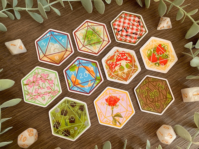 May include: A collection of nine hexagonal stickers featuring illustrations of twenty-sided dice, each with unique designs including koi fish, strawberries, a red rose, cherry blossoms, mushrooms, ants on a picnic blanket, and bear paw prints.