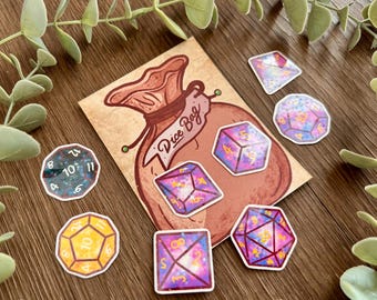 May include: A rectangular card featuring a brown illustration of a drawstring pouch with the text Dice Bag, surrounded by several die-cut stickers of multi-sided dice in various colors including purple, pink, yellow, and dark blue with numbers.