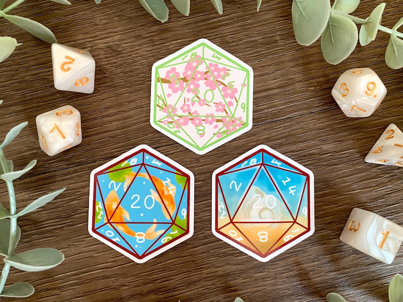 May include: Three die-cut stickers shaped like twenty-sided dice. The top sticker features pink cherry blossoms on a light background. The bottom left sticker shows orange koi fish in blue water. The bottom right sticker depicts a seashell on sand.