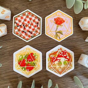 May include: Four hexagonal stickers featuring 20-sided die designs. One shows a red and white gingham pattern with ants, one a red rose, one red strawberries, and one red and white mushrooms. Several white polyhedral dice are scattered around.