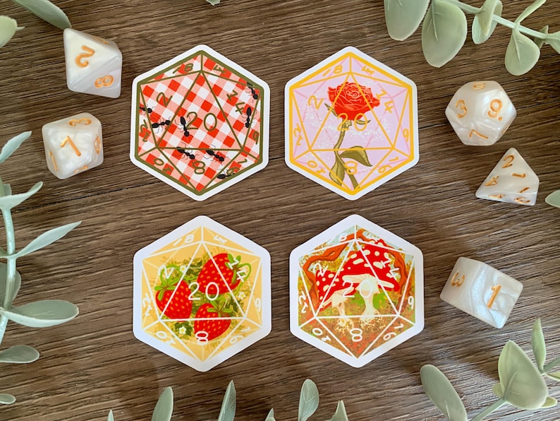 May include: Four hexagonal stickers featuring 20-sided die designs. One shows a red and white gingham pattern with ants, one a red rose, one red strawberries, and one red and white mushrooms. Several white polyhedral dice are scattered around.