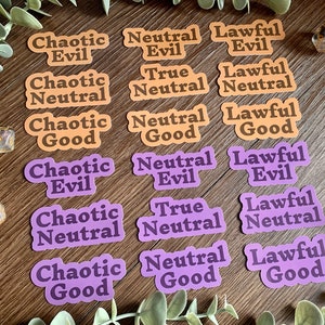 Peut inclure: Ensemble d'autocollants avec des termes d'alignement de Donjons et Dragons en orange et violet. On peut lire des phrases comme "Chaotique Mauvais", "Neutre Bon" et "Loyal Neutre". Des dés et une clé décorative sont également présents.