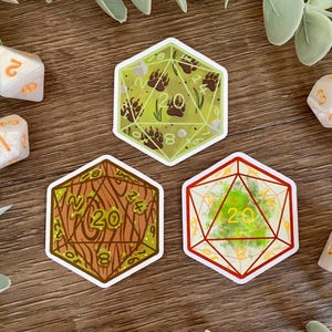 May include: Three hexagonal stickers shaped like twenty-sided dice. One sticker features a light green background with brown bear paw prints. Another shows a brown wood grain pattern. The third displays a bright green mossy texture inside red lines.