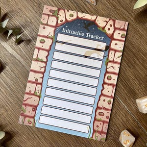 May include: An initiative tracker card with a stone arch design. The card has a blue background with white lines for tracking. The top of the card reads "Initiative Tracker". Dice and greenery are scattered around the card.