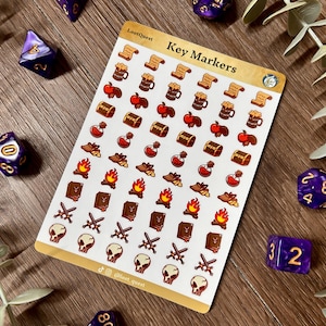 Puede incluir: Una hoja de pegatinas rectangular titulada Key Markers que presenta filas de pequeños iconos de temática fantástica, incluyendo pergaminos, jarras, manzanas, cofres del tesoro, pociones, oro, hogueras, libros, espadas cruzadas y calaveras.