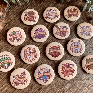 Op de afbeelding: Een verzameling van vijftien ronde houten tokens, elk met een andere fantasy-rollenspelklasse. De tokens hebben een lichtbruine achtergrond met kleurrijke illustraties en klassennamen zoals "Rogue", "Wizard" en "Barbarian" geschreven op banners.