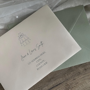 May include: Cream-coloured envelope with a wedding illustration and text. The envelope features the names "Jane & Lewis Smith" and an address. A sage green envelope is partially visible behind the cream envelope.