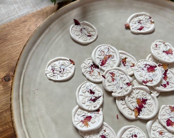 Puede incluir: Un plato de sellos de cera blanca con un diseño floral y acentos rojos y naranjas. Los sellos están esparcidos en un plato blanco.