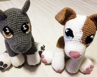 May include: Two crocheted stuffed toys, one grey with white paws and one white with brown and pink accents. Both have black eyes with white pupils and are sitting on a white surface.