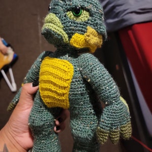 Peut inclure: Poupée créature au crochet faite à la main, dans des tons de vert et de jaune. La poupée a de grands yeux verts expressifs, une tête texturée et une poitrine jaune. Les bras et les jambes sont également crochetés, avec des mains et des pieds en forme de griffes. Objet unique et artisanal.