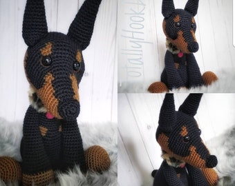 May include: A crocheted plush toy dog in black and brown with a pink tongue sticking out. The dog is sitting on a fluffy white surface. The text "TOTALLYHOOKD" is visible in the bottom left corner of the image.